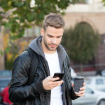 Un ragazzo tiene in mano un caffè e usa un telefono